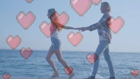 Multiple-red-heart-icons-floating-against-caucasian-couple-holding-hands-walking-near-the-sea