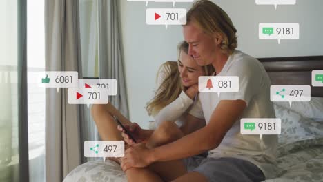 Animation-of-social-media-notifications-over-smiling-couple-sitting-on-bed-using-smartphone