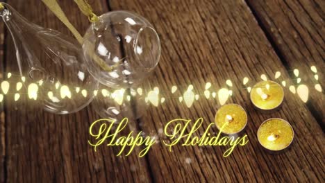Animation-of-text,-happy-holidays,-in-yellow,-over-string-lights,-baubles-and-candles-on-wood-floor