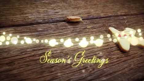Animation-of-text,-season's-greetings,-in-yellow,-over-string-lights-and-falling-gingerbread-man