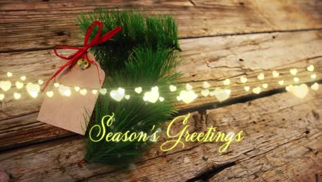 Animation-of-text,-season's-greetings,-in-yellow,-over-string-lights-and-christmas-sprig-and-label