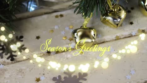 Animation-of-text,-season's-greetings,-in-yellow,-over-string-lights-and-christmas-tree-decorations