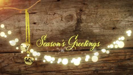 Animation-of-text,-season's-greetings,-in-yellow,-over-string-lights-and-christmas-bell-decoration