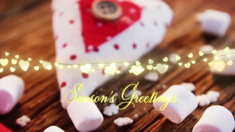 Animation-of-text,-season's-greetings,-with-string-lights,-marshmallows-and-christmas-decorations
