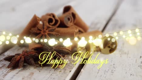 Animation-of-text,-happy-holidays,-in-yellow,-over-string-lights-and-cinnamon-sticks-on-floorboards