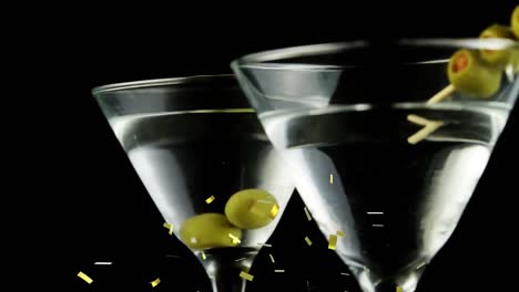 Animation-of-confetti-falling-over-cocktail-glasses-with-olives-on-black-background
