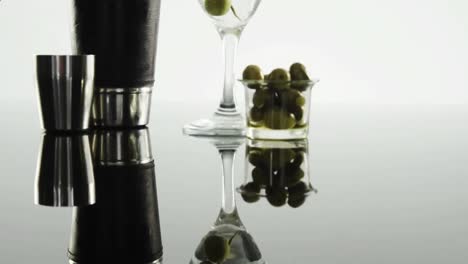 Animation-of-red-shapes-moving-over-glass-of-wine-and-olives-on-white-background