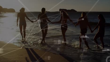 Animation-of-network-of-connections-over-female-friends-holding-hands-on-beach