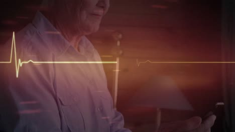 Leuchtender-Roter-Herzfrequenzmesser-Gegen-Kaukasische-ältere-Frau,-Die-Zu-Hause-Ihr-Smartphone-Benutzt