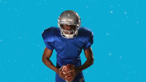 Animation-of-snow-falling-over-american-football-player-with-ball-on-blue-background