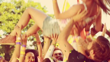 Animation-of-gold-confetti-falling-over-happy-woman-being-thrown-in-air-by-friends-outdoors