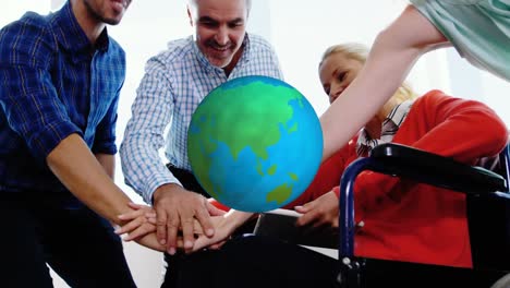 Animation-of-globe-rotating-over-smiling-diverse-colleagues-stacking-hands-at-casual-office-meeting