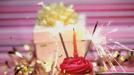 Animation-Von-Goldenem-Konfetti-über-Der-Hand,-Das-Eine-Streichholzkerze-Und-Wunderkerzen-Auf-Einem-Geburtstags-Cupcake-Hält