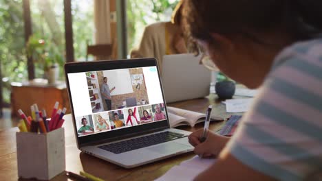 Girl-doing-homework-and-having-a-video-conference-with-teacher-and-classmates-on-laptop-at-home