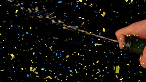 Confetti-falling-over-mid-section-of-person-spraying-champagne-against-black-background