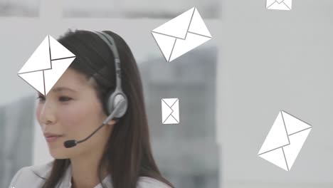Message-icons-falling-over-asian-female-customer-care-executive-talking-on-phone-headset-at-office