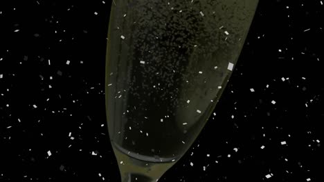 Confetti-falling-over-close-up-of-champagne-bubbles-in-a-glass-against-black-background