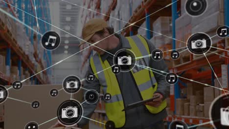 Network-of-digital-icons-against-male-worker-using-digital-tablet-and-checking-stock-at-warehouse