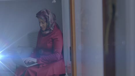 Animación-Del-Mapa-Mundial-Sobre-Una-Mujer-Asiática-Con-Hijab-Sentada-Y-Usando-Una-Computadora-Portátil