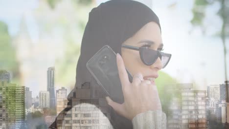 Animación-De-Una-Mujer-Asiática-Con-Hijab-Y-Gafas-De-Sol-Usando-Un-Teléfono-Inteligente-Sobre-El-Paisaje-Urbano