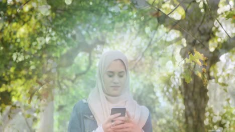 Animation-of-asian-woman-in-hijab-using-smartphone,-over-forest