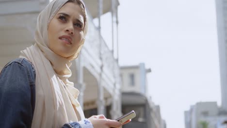 Animation-Einer-Asiatischen-Frau-Im-Hijab,-Die-über-Der-Stadtlandschaft-Sitzt-Und-Ihr-Smartphone-Benutzt
