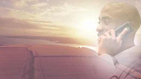 Animation-Eines-Lächelnden-Afroamerikanischen-Mannes,-Der-Sein-Smartphone-über-Einer-Sonnenuntergangslandschaft-Benutzt