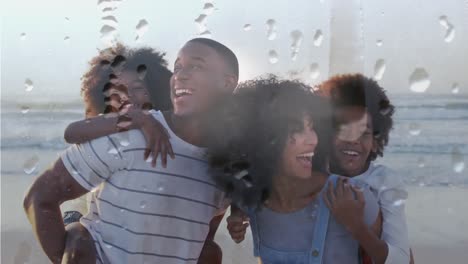 Animation-Von-Tröpfchen-über-Einer-Glücklichen-Afroamerikanischen-Familie-Am-Strand-An-Einem-Sonnigen-Tag,-Die-über-Das-Meer-Lächelt