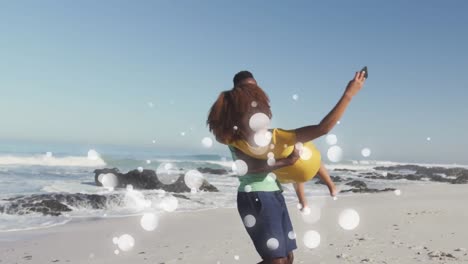 Animation-of-happy-african-american-couple-having-fun-at-beach-using-smartphone,-over-white-spots