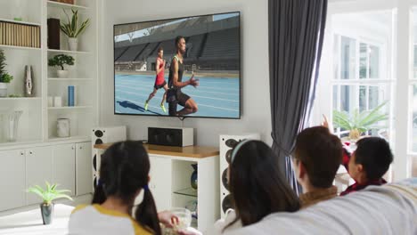 Composite-of-happy-family-sitting-at-home-together-watching-athletics-running-on-tv