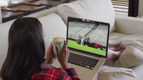 Composite-of-woman-sitting-at-home-holding-coffee-watching-rugby-match-on-laptop