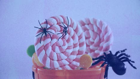 Animation-Von-Plastikspinnen-Auf-Orangefarbenem-Kürbiseimer-Voller-Süßigkeiten,-Auf-Fliederfarbenem-Hintergrund
