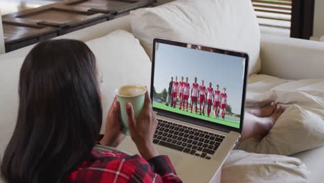 Composite-of-woman-sitting-at-home-holding-coffee-watching-hockey-match-on-laptop