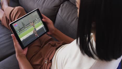 Composite-of-woman-sitting-at-home-on-couch-watching-athletics-high-jump-event-on-tablet