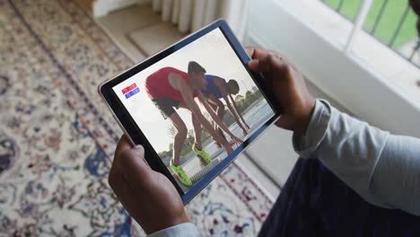 Composite-of-man-sitting-at-home,-watching-athletics-running-event-on-tablet