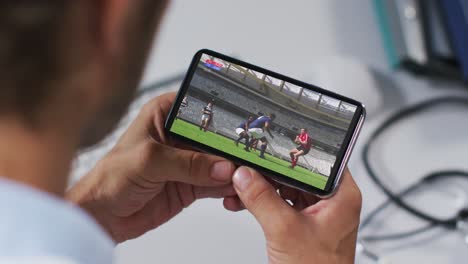 Composite-of-male-doctor-watching-rugby-match-on-smartphone