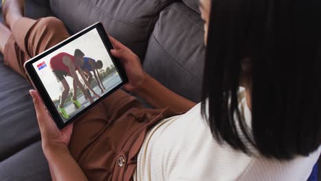 Composite-of-woman-sitting-at-home-on-couch-watching-athletics-running-event-on-tablet