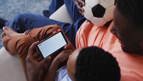Zusammensetzung-Aus-Vater-Und-Sohn,-Die-Zu-Hause-Ein-Fußballspiel-Auf-Dem-Smartphone-Ansehen