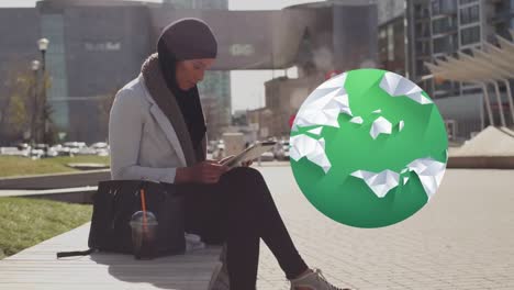 Globe-and-multiple-heart-icons-floating-over-woman-in-hijab-using-digital-tablet-on-the-street