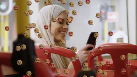 Animación-De-Emojis-Que-Caen-Sobre-Una-Mujer-Con-Hijab-Usando-Un-Teléfono-Inteligente