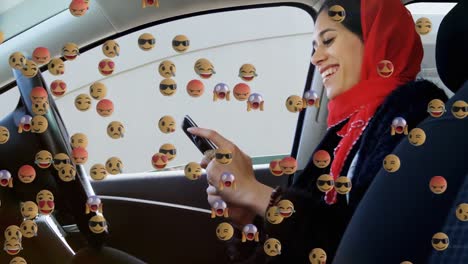 Animation-of-od-falling-emojis-over-woman-in-hijab-using-smartphone