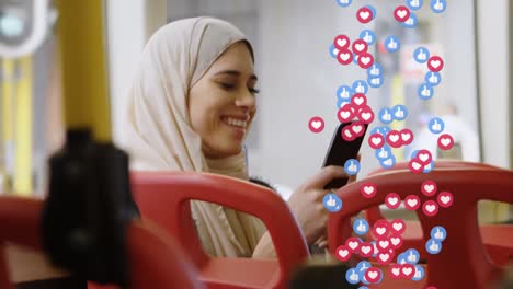 Animación-De-Iconos-De-Redes-Sociales-Que-Caen-Sobre-Una-Mujer-Con-Hijab-Usando-Un-Teléfono-Inteligente