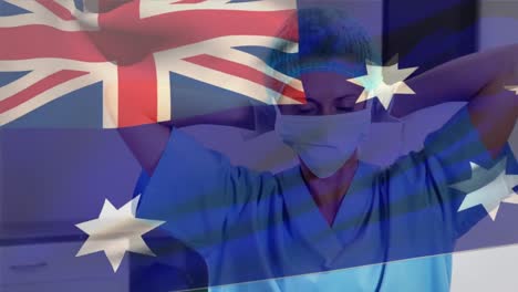 Australia-flag-waving-against-caucasian-female-health-worker-wearing-face-mask-at-hospital