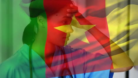 Cameroon-flag-waving-against-stressed-african-american-female-health-worker-at-hospital