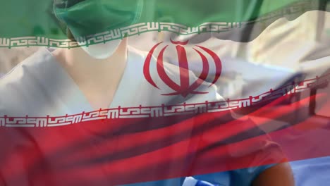 Bandera-De-Irán-Ondeando-Contra-Una-Trabajadora-De-Salud-Caucásica-Que-Usa-Mascarilla-En-El-Hospital