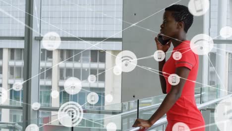Netzwerk-Digitaler-Symbole-Gegen-Afroamerikanische-Geschäftsfrau,-Die-Im-Büro-Auf-Dem-Smartphone-Spricht