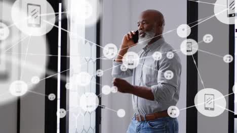 Network-of-digital-icons-against-african-american-senior-businessman-talking-on-smartphone-at-office