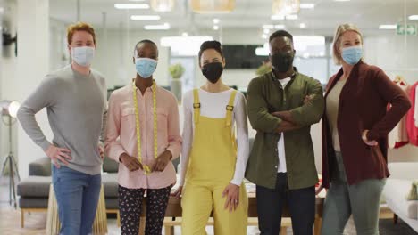 Diverse-group-of-male-and-female-business-colleagues-wearing-face-masks-and-looking-at-camera