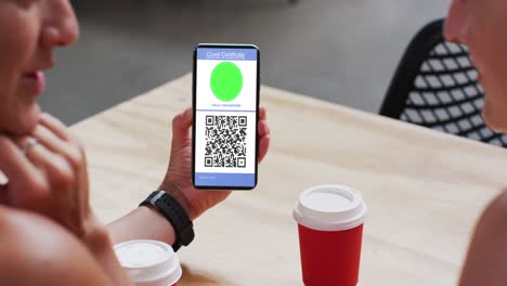 Man-at-cafe-showing-smartphone-with-covid-vaccination-certificate-and-qr-code-on-screen