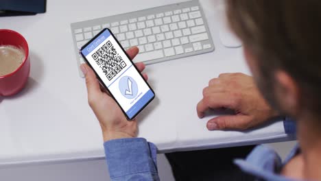Man-at-desk-holding-smartphone-with-covid-vaccination-certificate,-tick-and-qr-code-on-screen